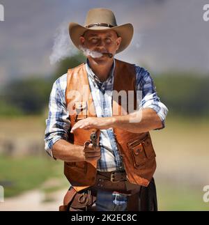 Hes the wrangler of beasts. A mature cowboy outdoors with his gun drawn. Stock Photo