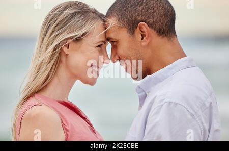 Portrait of couple at the beach with their forehead touching. Multiracial man and woman in relationship, happy, smiling and in love on vacation Stock Photo
