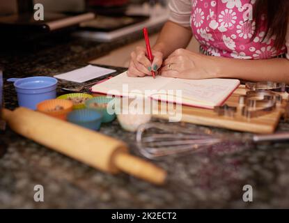 Shes about to bake some tasty treats. Shot of a woman writing in a recipe book. Stock Photo