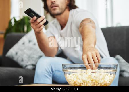 I could eat this entire bowl with no one watching. Shot of man sitting on the couch eating popcorn and watching tv. Stock Photo