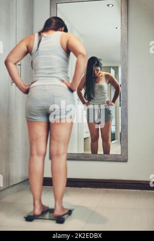 Keeping a close eye on her weight. Shot of a young woman weighing herself on a scale at home. Stock Photo