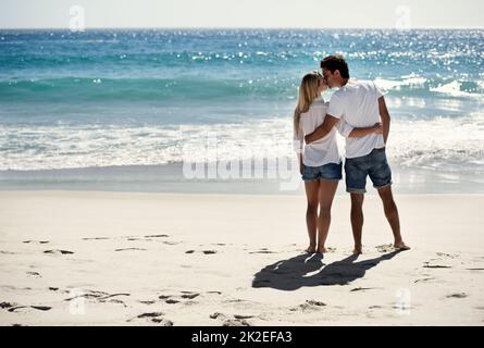 A loving moment in a peaceful place. A happy couple kissing on the beach with copyspace. Stock Photo
