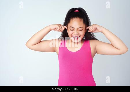 No...no...NOOO. Studio shot of a cute young girl with her fingers in her ears against a gray background. Stock Photo