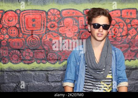 Portrait of an urban artist. Portrait of a stylish young man standing in front of a graffiti filled wall. Stock Photo