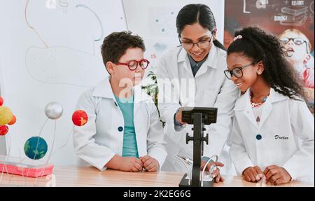 Lets take a closer look at this. Shot of a young science teacher using a microscope with her pupils in science class at school. Stock Photo