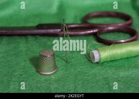 Spool of Green Thread, Thimble and Needle on Green Fabric Stock Photo