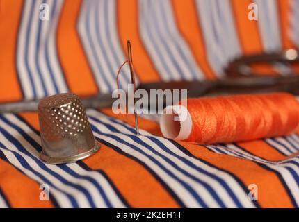 Spool of Orange Thread and Thimble on Orange and White Fabric Stock Photo