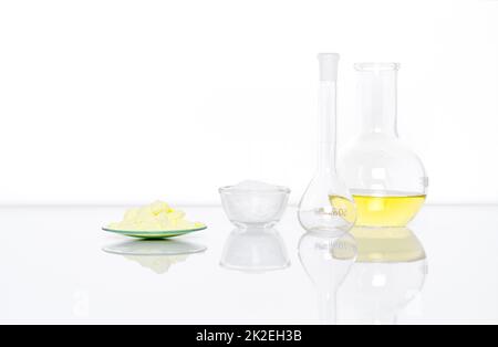Sulfur Powder in Chemical Watch Glass place next to White flake chemical in glass container, Volumetric flask and Aluminium chloride liquid in Flat Bottom Flask.  Side View Stock Photo