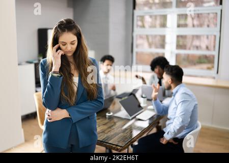 Stressed Female Colleague And Other Workers Bullying Stock Photo