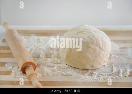 Close-up of rolling pin and dough on wooden table with flour. Basic needs and rising of prices concept. Stock Photo