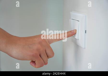 Wastage of Energy. Female finger is turn off on lighting switch. Stock Photo