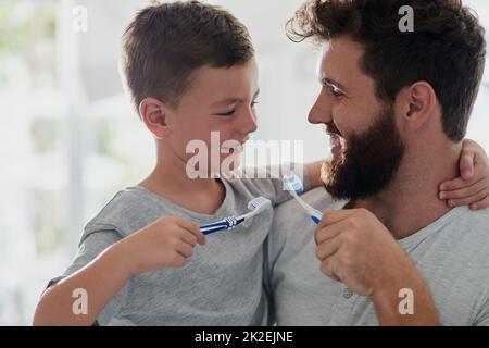 Got to keep the tooth decay at bay. Shot of a father and his little son brushing their teeth together in the bathroom at home. Stock Photo