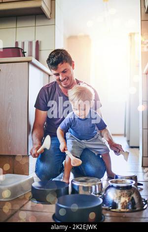 Daddys little noise maker. Shot of a father watching his young son as he plays drums on pots on the kitchen floor. Stock Photo