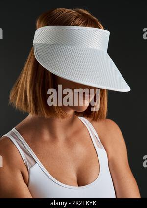 You wont see me on the court without my visor. Cropped shot of a sporty young woman wearing a sun visor against a dark background. Stock Photo