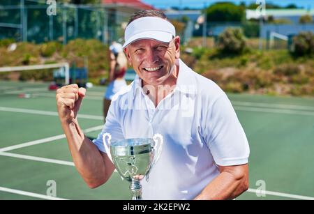 Hard work always pays off. Cropped portrait of a handsome mature man holding up a trophy after winning a tennis match during the day. Stock Photo