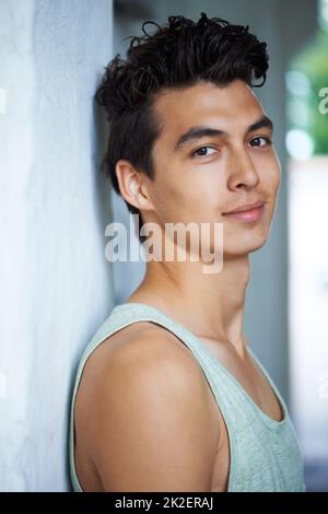 Youthful good looks. A handsome young man smiling at you while leaning against a wall. Stock Photo