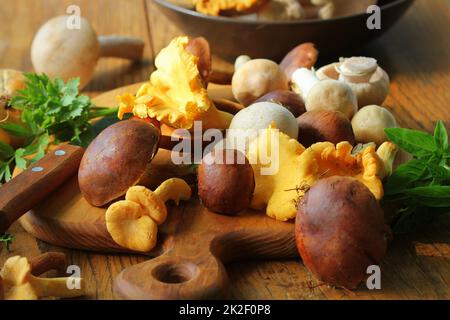 Mix of forest mushrooms on cutting board over old wooden table Stock Photo