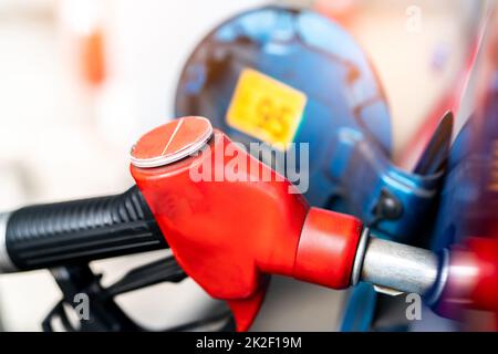 Close-up red fuel nozzle. Gasoline pump nozzle. Car fueling at gas station. Refuel fill up with petrol gasoline. Petrol pump filling fuel nozzle in fuel tank of car at gas station. Oil price crisis. Stock Photo