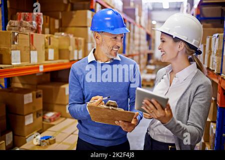 Orders sorted. Shot of two managers looking at stock in a large warehouse. Stock Photo