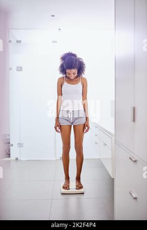 Now thats what I like to see. Shot of an attractive young woman weighing herself on a scale in the bathroom at home. Stock Photo