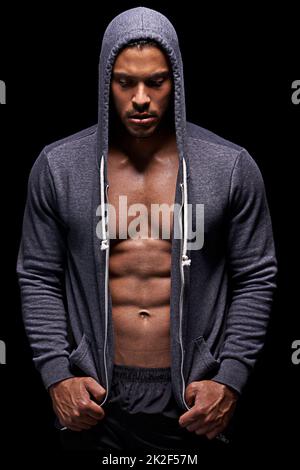 Getting his fitness on. Studio shot of a muscular young man wearing a hoodie isolated on black. Stock Photo