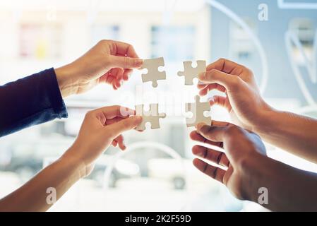 Looking for their perfect fit. Shot of a group of unidentifiable friends holding up puzzle pieces toegther. Stock Photo