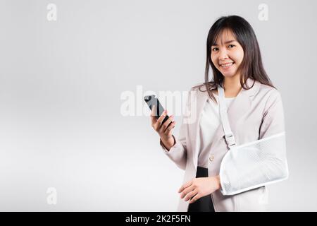 Woman confident smiling broken arm after accident and wear arm splint for treatment and hold smartphone Stock Photo