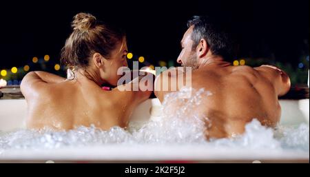 Were back in the swing of things. Rearview shot of an affectionate mature couple relaxing in a hot tub together at night. Stock Photo