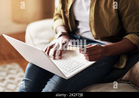 I could really use a good bargain right now.... Cropped shot of an unrecognizable man using a laptop and a credit card to shop online while sitting on his couch at home. Stock Photo