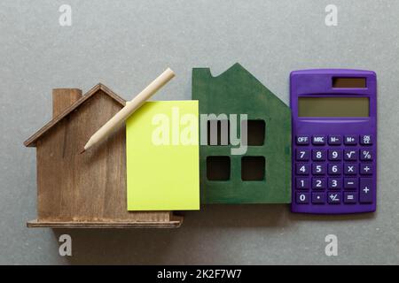 Wooden house model and blank memo pad, calculator on gray background. Real estate concept. top view, copy space Stock Photo