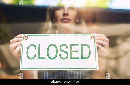 Sorry were closed. Shot of a woman putting up a closed sign in a bar. Stock Photo
