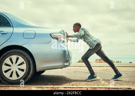 Sometimes youve gotta get out and push. Full length shot of a young man pushing his car along the road after breaking down. Stock Photo