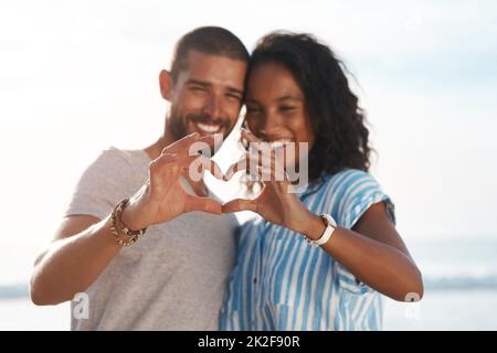 Your heart is held close to mine. Shot of a young couple making a heart shape with their hands at the beach. Stock Photo