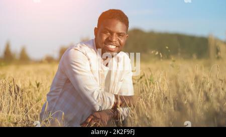 African American agriculturist sits on wheat field smiling Stock Photo