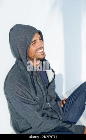 Happy to hangout. A handsome young man sitting on the floor and smiling while wearing a hoodie. Stock Photo