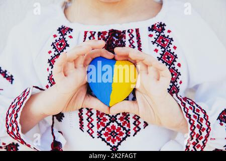 Girl in embroidery or embroidered shirt hold heart shape with Ukrane flag Stock Photo