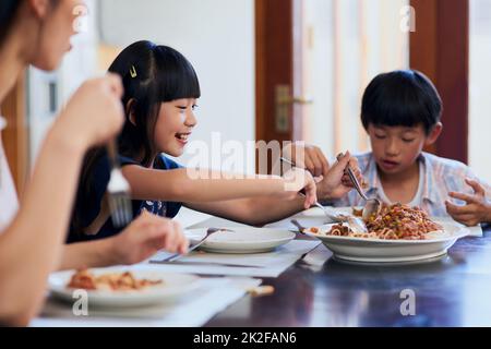 Im going in for seconds. Shot of two little children enjoying a meal with their mother at home. Stock Photo