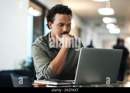 I know I can make this better. Shot of a handsome young businessman sitting alone in the office and looking contemplative while using his laptop. Stock Photo