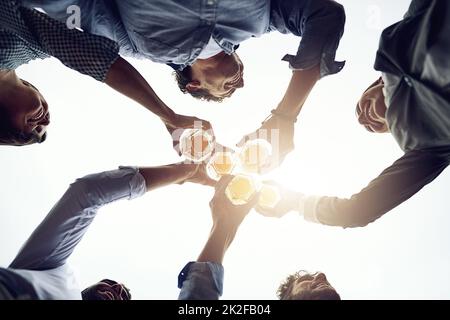 What a year its been. Low angle shot of a group of cheerful young work colleagues forming a huddle and having a celebratory toast with beer outside during the day. Stock Photo