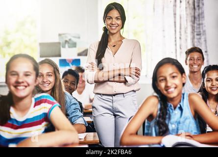 Their favourite class with their favourite teacher. Portrait of an attractive young teacher standing with her arms folded in a classroom. Stock Photo
