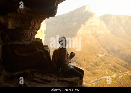 The memories are worth the climb. Shot of a woman taking a picture with her camera on top of a mountain. Stock Photo