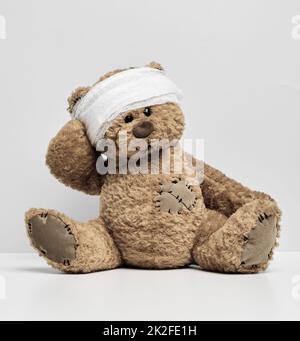 Children's toy teddy bear sits with a bandaged head. Childhood trauma concept Stock Photo