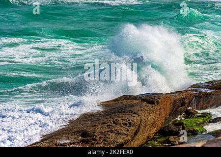 Wave breaking over rocks with water splashing in the air Stock Photo