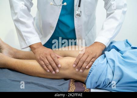 Asian doctor physiotherapist examining, massaging and treatment knee and leg of senior patient in orthopedist medical clinic nurse hospital. Stock Photo