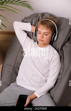 Relaxed teenager sitting on frameless beanbag chair with headphones. White t-shirt mockup Stock Photo