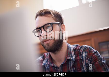 Using all the latest tech. a handsome young hipster working on a laptop. Stock Photo