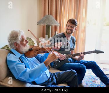 Bonding through their music. Shot of a young man playing the electric guitar while his elderly grandfather plays the violin on the couch. Stock Photo