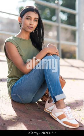 I just felt like being out in the city. Full length portrait of an attractive young woman looking serious while sitting in the city. Stock Photo