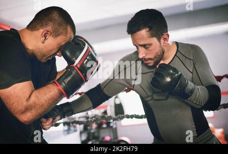 Put your hands up. Shot of two young male boxers facing each other in a training sparing match inside of a boxing ring at a gym during the day. Stock Photo