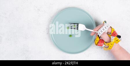 One single pea on a plate, hand with tape measure and fork, diet and loosing weight concept, healthy lifestyle Stock Photo
